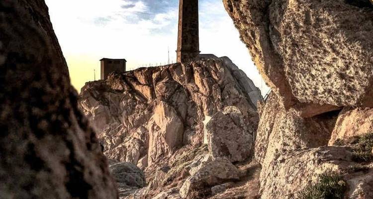 Torre de faro de piedra encaramada en acantilados costeros dramáticos enmarcados por grandes rocas a la hora dorada