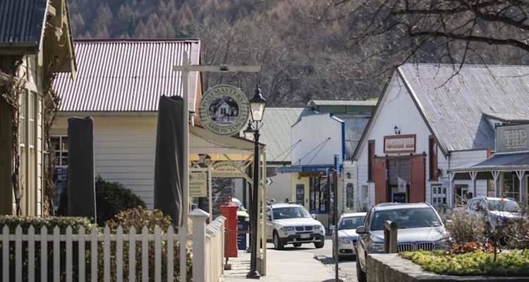 Une charmante rue principale historique bordée de clôtures à piquets, de bâtiments patrimoniaux et de voitures garées par une belle journée ensoleillée.