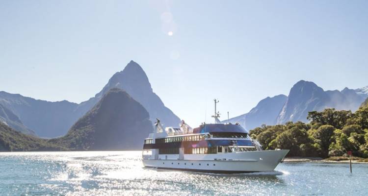 Un bateau de croisière blanc glisse sur les eaux scintillantes du Milford Sound sous des pics de granit imposants.