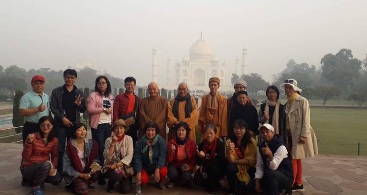 Eine Gruppe von Reisenden steht mit dem nebelverhangenen Taj Mahal im Hintergrund während des frühen Morgenlichts.