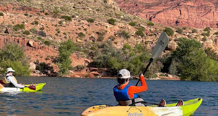 Deux kayakistes pagaient sur un lac bleu calme encadré par des falaises désertiques rouges et escarpées.
