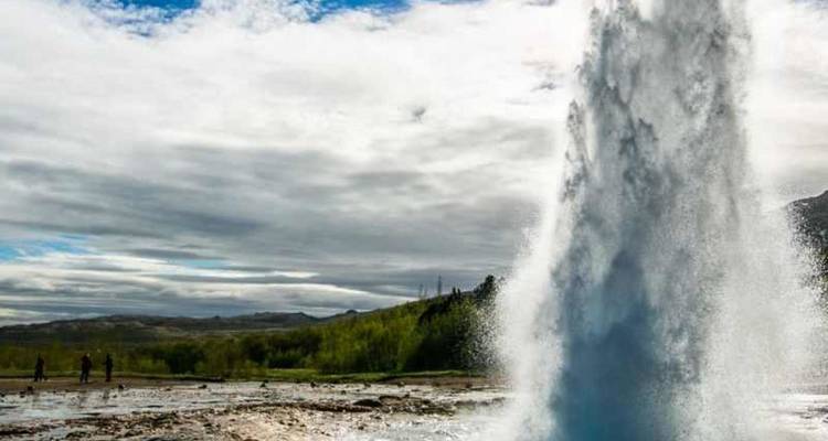 Un grand geyser se déchaîne vers le ciel en libérant de la vapeur sous un ciel partiellement nuageux dans un paysage géothermique