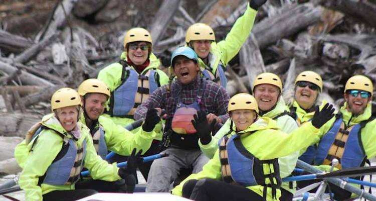 Grupo alegre con chaquetas de neón sentado en una balsa de aguas blancas listo para lanzarse en un río de montaña