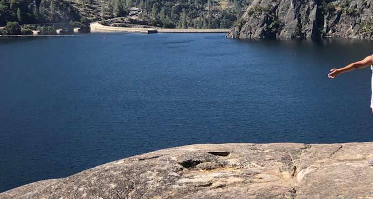 Un visiteur se tient sur une corniche de granit surplombant un réservoir bleu profond bordé par des falaises boisées.