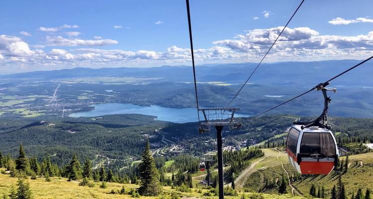 El teleférico asciende sobre laderas boscosas hacia un extenso lago y un paisaje rural de retazos.