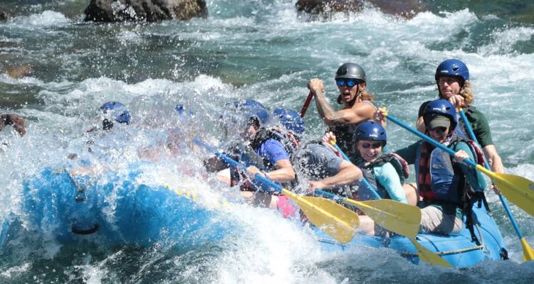 Un equipo de rafting en aguas blancas lucha contra los rápidos turbulentos, con los remos levantados en medio de las olas que salpican.
