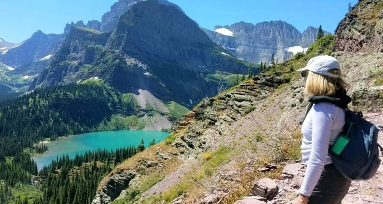 Un excursionista mira hacia un lago alpino de color turquesa anidado bajo picos rocosos dramaticos.