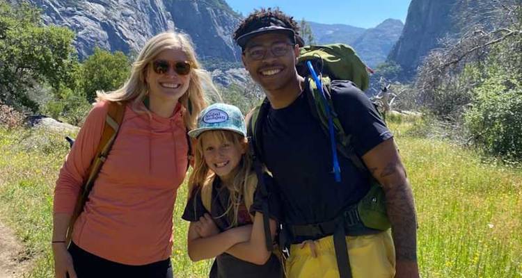 Une famille souriante pose sur un sentier herbeux avec les falaises granitiques de Yosemite en arrière-plan.