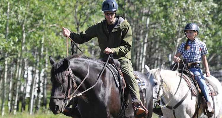 Un adulto y un niño pasean a caballo por un exuberante bosque de álamos.