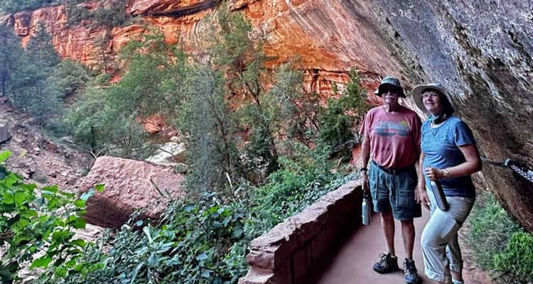 Deux randonneurs s'arrêtent sous une falaise surplombante aux parois rocheuses rougeoyantes à Zion.