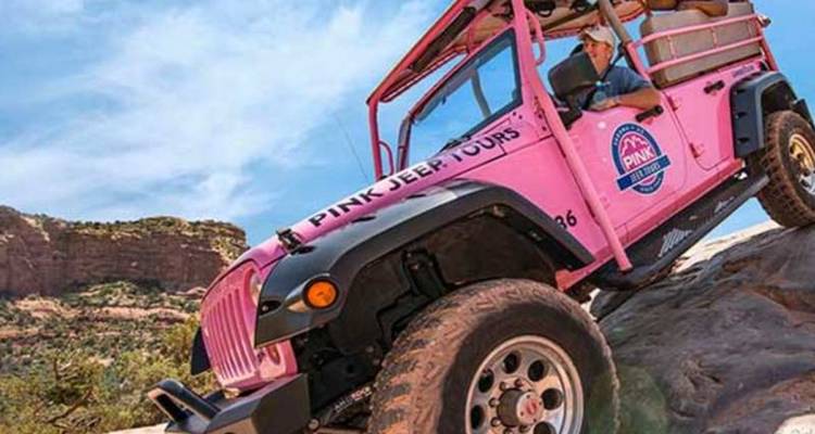Un jeep rose vif grimpe une pente rocheuse rouge escarpée sous un ciel désertique ensoleillé.