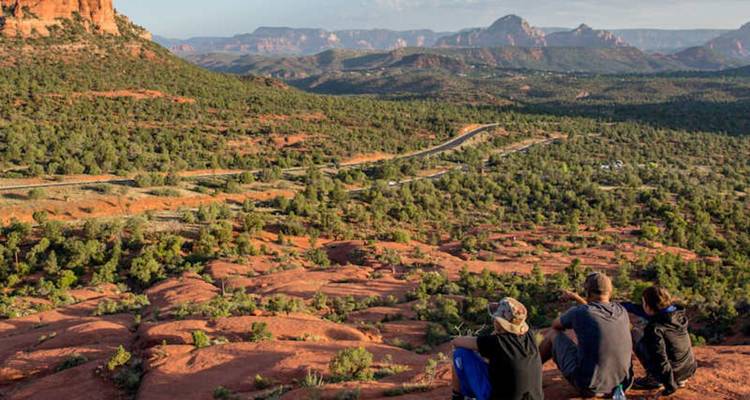 Trois amis sont assis sur un belvédère de roches rouges, admirant les vues panoramiques des mesas de Sedona et des routes sinueuses.