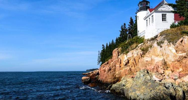 Le phare blanc classique se dresse au sommet de falaises de granit rose escarpées surplombant les eaux bleu profond de l'Atlantique.