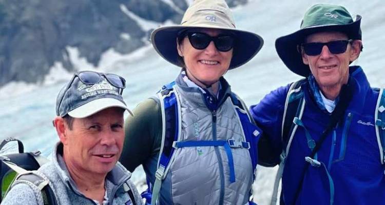 Trois trekkeurs en équipement de glacier sourirent avec des crevasses bleu glace derrière eux.