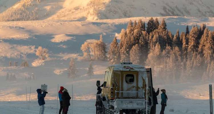 Les visiteurs se tiennent près d'un véhicule jaune tout-terrain spécialisé pour la neige, avec des montagnes givrées brillant à la lumière de l'aube.