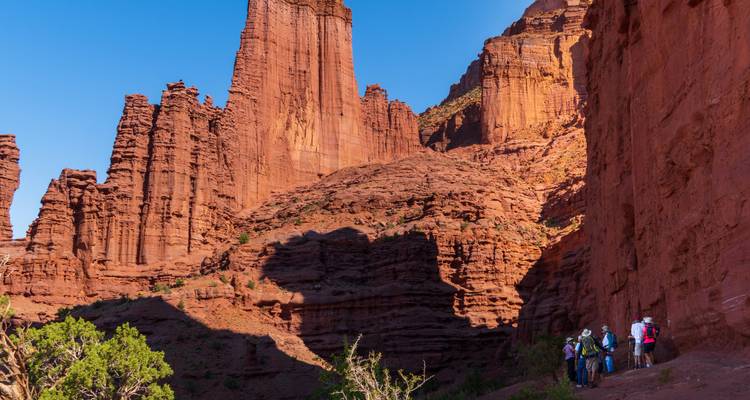 Les randonneurs marchent parmi les imposantes aiguilles de grès rouge et les parois de canyon sous un ciel bleu dégagé.