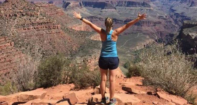 Un randonneur lève les bras en signe de triomphe au-dessus d'un vaste gouffre de roches rouges du Grand Canyon.