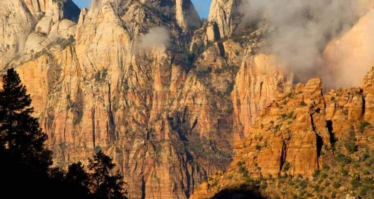 Les murs imposants de grès orange se dressent dans les nuages bas tandis que la lumière du matin illumine le canyon de Zion.