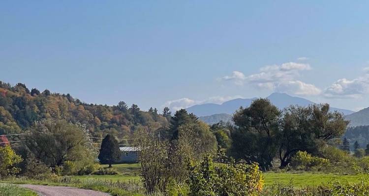 Vallée pastorale avec des collines ondulantes et des montagnes lointaines sous un ciel bleu dégagé.