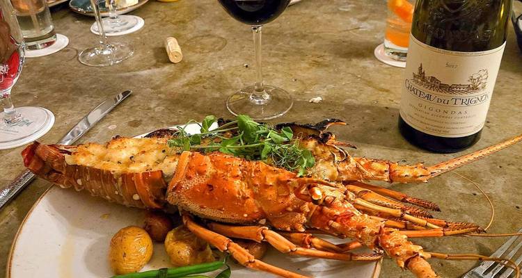 Gegrilde kreeft geserveerd op een bord met baby aardappeltjes en groenten, vergezeld van een fles en glas rode wijn op een restauranttafel