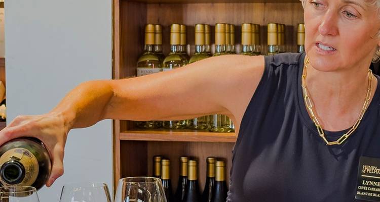 Un sommelier verse du vin blanc dans des verres de dégustation à l'intérieur d'une cave tapissée de bouteilles.