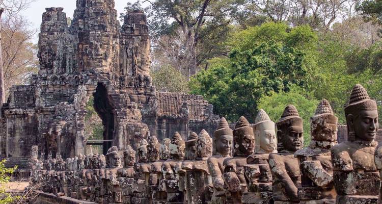 Stone statues line the causeway leading to the imposing South Gate of Angkor Thom amid jungle greenery