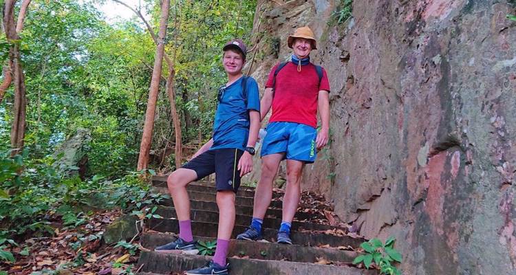 Two young hikers stand on ancient stone steps surrounded by dense tropical forest