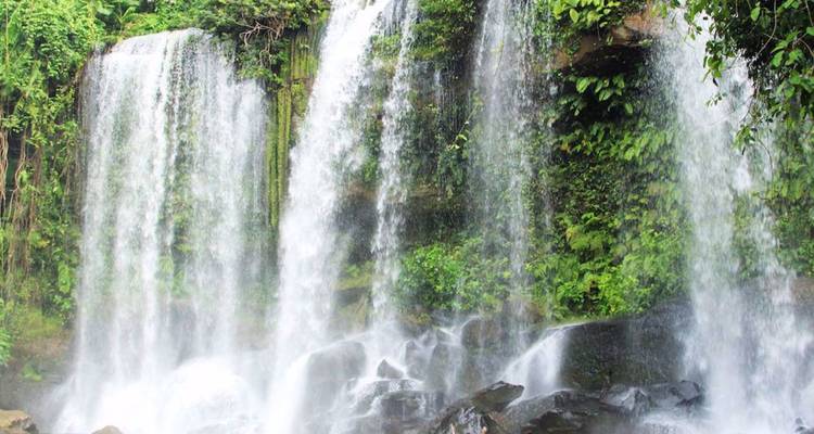 Multiple streams of water cascade over a lush green cliff creating a tropical waterfall