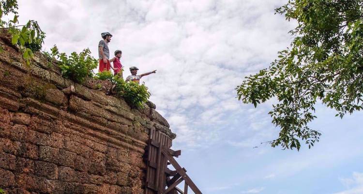 Small group stands atop an ancient temple wall, one person pointing toward the horizon under fluffy clouds.