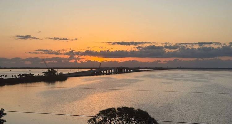 Oranje zonsopgang boven een kustbaai met een lange brug die zich uitstrekt naar de horizon.