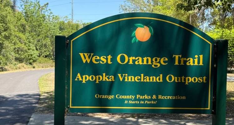 Groen bord dat het West Orange Trail markeert bij Apopka Vineland Outpost naast het geasfalteerde pad.