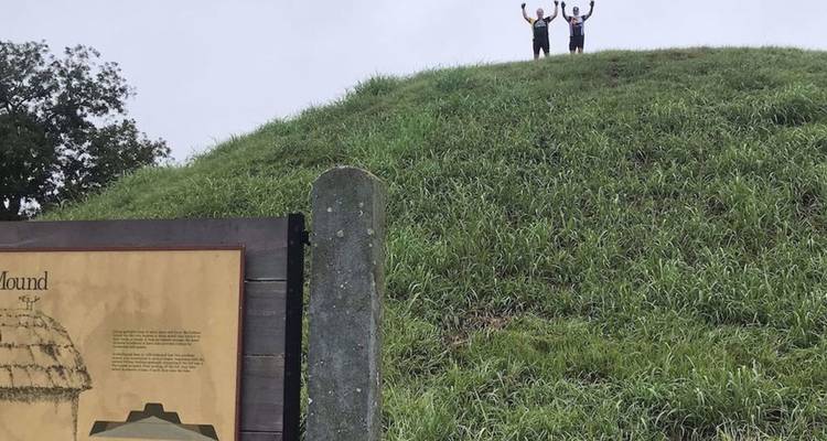 Twee wandelaars die juichen op de top van een graszode ceremoniele heuvel op een bewolkte dag.