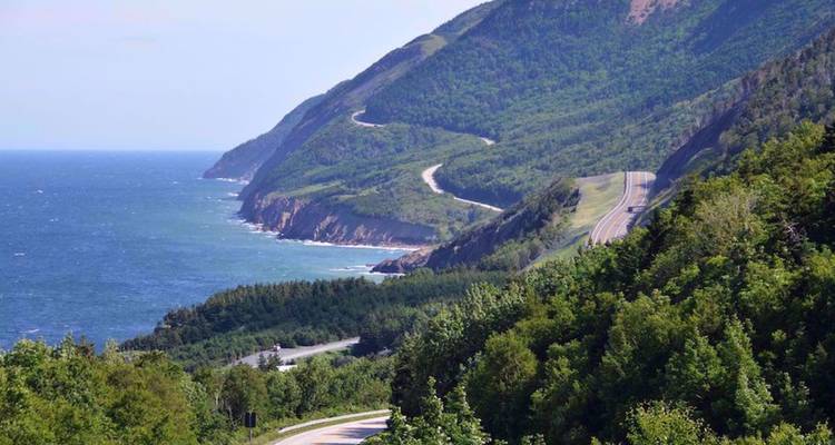 Une route sinueuse de style Cabot Trail serpente à travers des terres boisées dominant l'océan bleu.