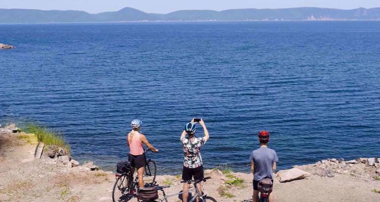 Trois cyclistes se tiennent près d'une côte rocheuse et prennent des photos de la vaste mer bleue.