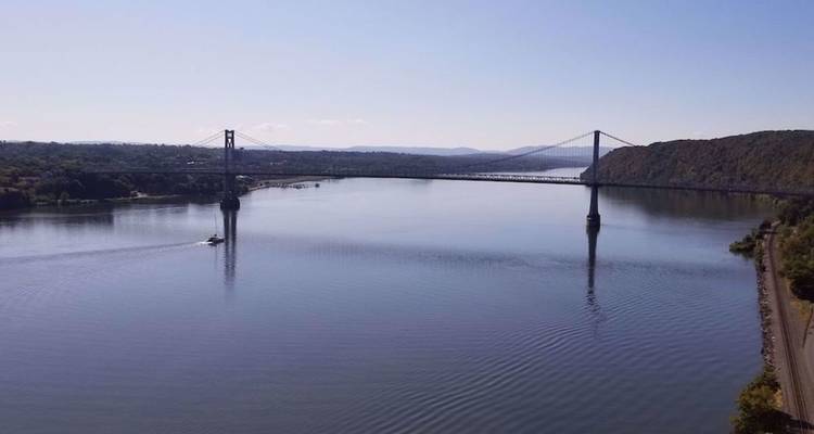 Brede rivier met een lange hangende brug die tussen bosrijke heuvels overspant