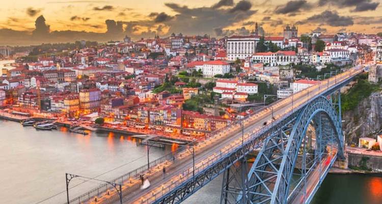 Sunset view of Porto with illuminated Dom Luís I Bridge spanning the Douro River and old town rooftops.