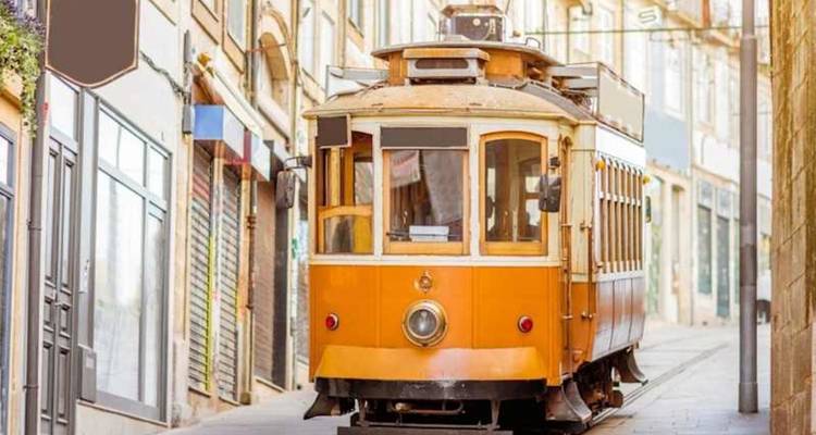 Vintage yellow tram on a narrow, sunlit cobblestone street flanked by historic buildings.