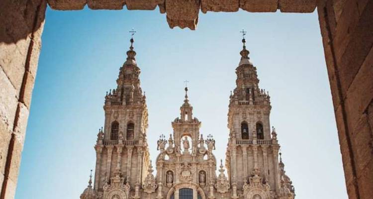 Twin bell towers of Santiago Cathedral framed by a stone archway against a clear sky.
