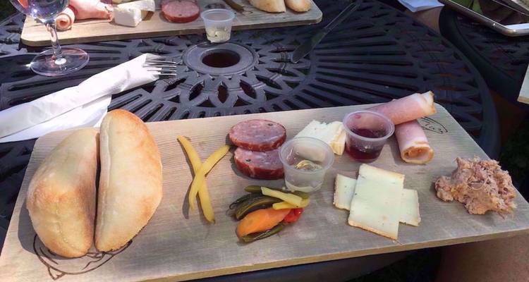 Plateau de charcuterie garni de pain, de viandes cuites, de fromage, de cornichons et de petits verre de dégustation sur une table en métal.