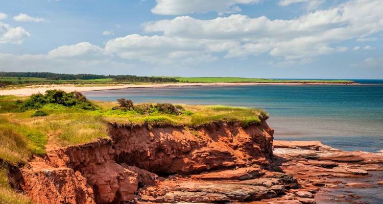 Les falaises de grès rouge s'élèvent au-dessus des eaux turquoise et des caps herbeux sous des nuages épars.