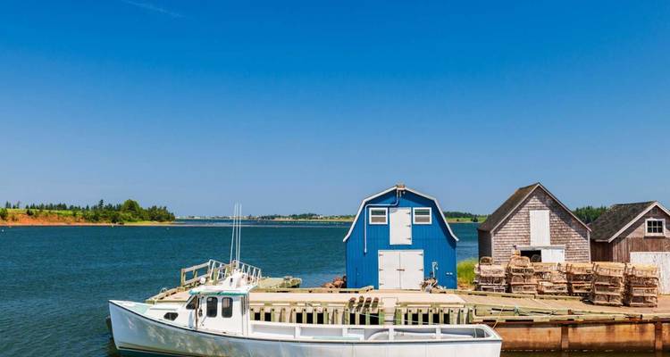 Des cabanes de pêche colorées et un bateau blanc reposent sur une baie calme sous un ciel dégagé.