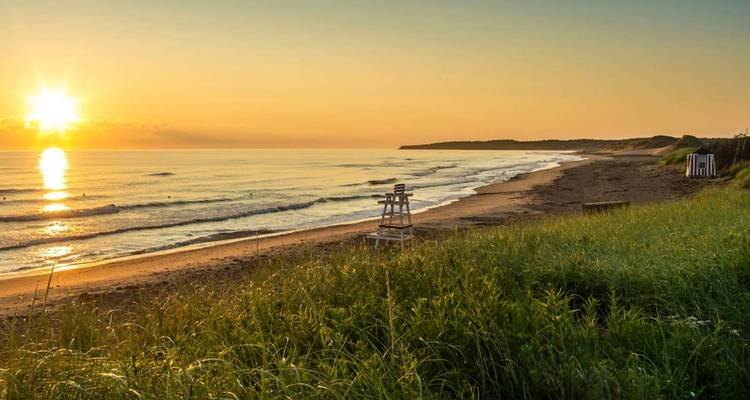 L'aube dorée projette une lumière chaleureuse sur une plage de sable tranquille et une chaise de maître-nageur.