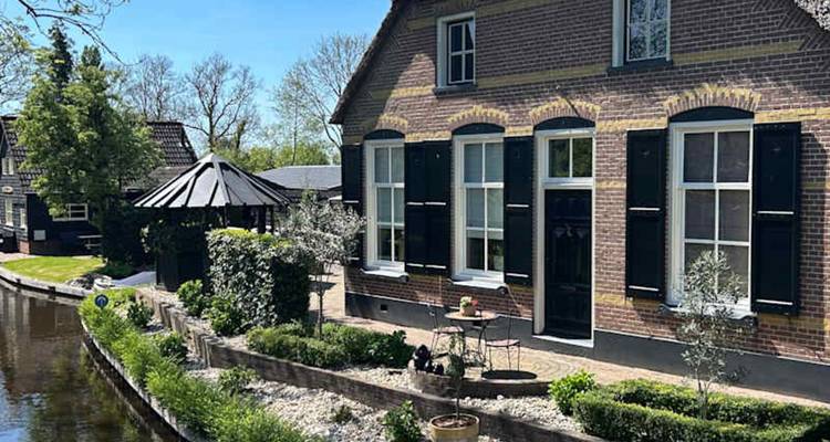 Charming canal-side brick house with shutters, garden seating and reflection in still water.