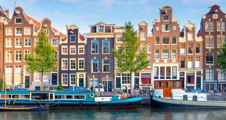 Classic row of narrow canal houses reflected in calm water on a clear day.