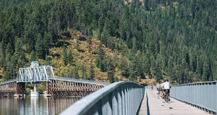 Les cyclistes parcourent un long pont-promenade enjambant un lac entouré d'une dense forêt de pins.