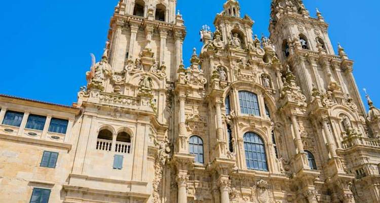 Ornate façade of the Cathedral of Santiago de Compostela glowing under a vivid blue sky.