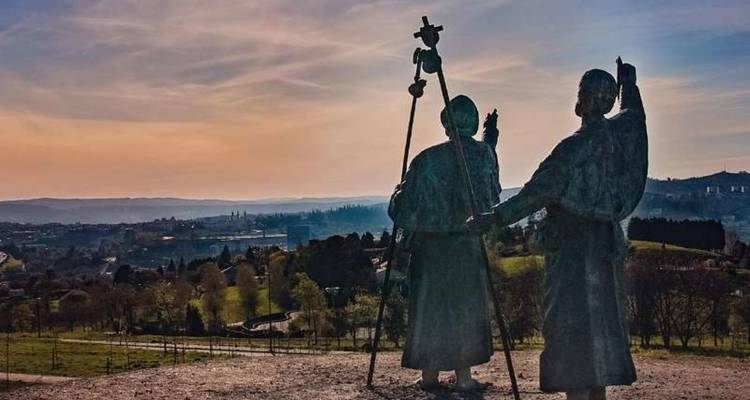 Silhouettes of two pilgrim statues overlooking sunset-lit landscape near Santiago.