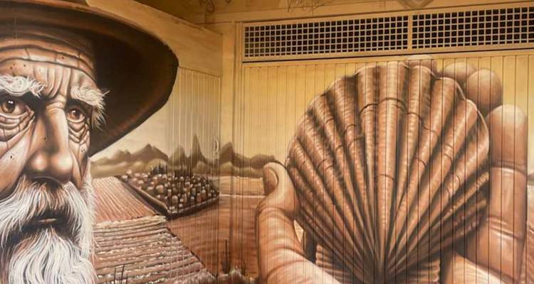 Street mural of an elderly pilgrim holding a scallop shell, symbol of the Camino.