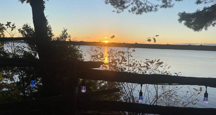 Gouden zonsondergang gezien door een rustieke houten hek en hangende snoeren met lampjes boven een rustig meer