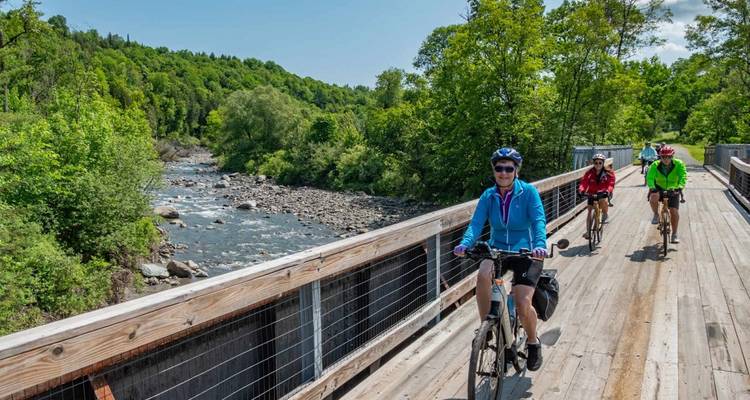 Fietsers steken een houten brug over boven een rotsachtige rivier die door een weelderig bos stroomt